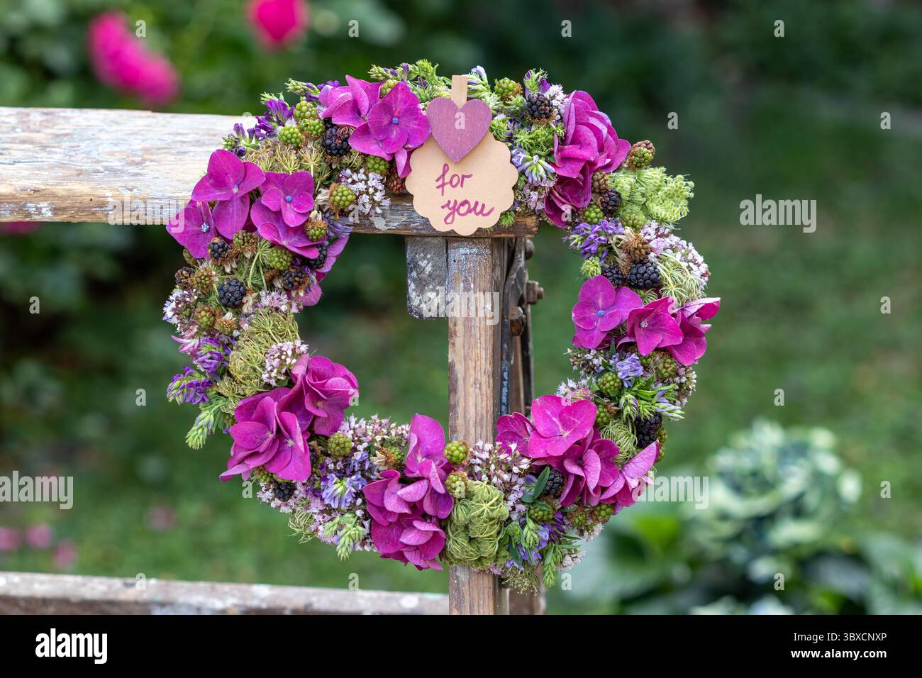 corona floreale con ortensie in fiore, carote selvatiche, timo selvatico, erba medica e more appese su una scala Foto Stock
