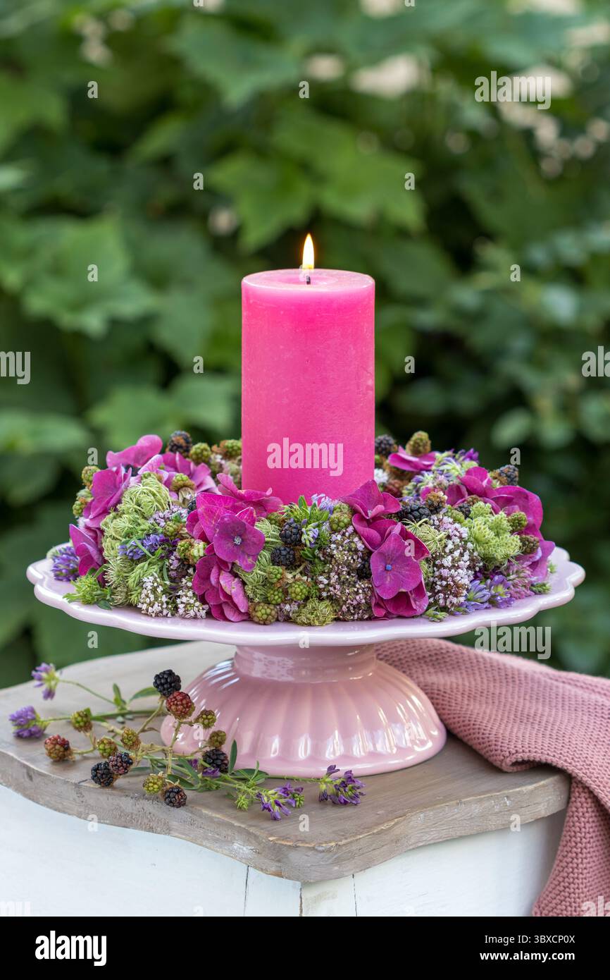 composizione con candela e corona floreale con ortensie in fiore, carote selvatiche, timo selvatico, erba medica e more Foto Stock