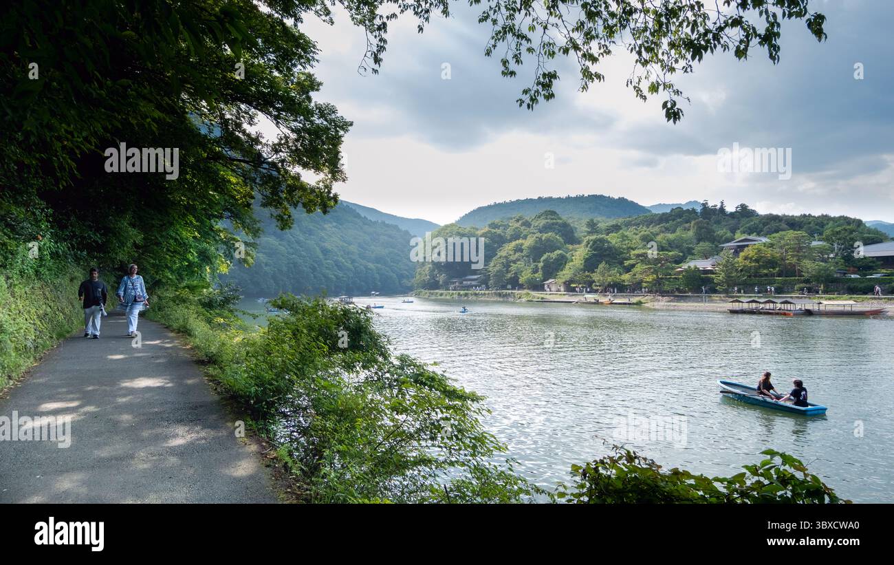 Un momento di pace lungo il fiume a Kyoto, in Giappone. Un uomo si siede tranquillamente vicino a una fila di barche blu mentre le tradizionali barche a remi e in legno si spostano lungo il fiume Foto Stock