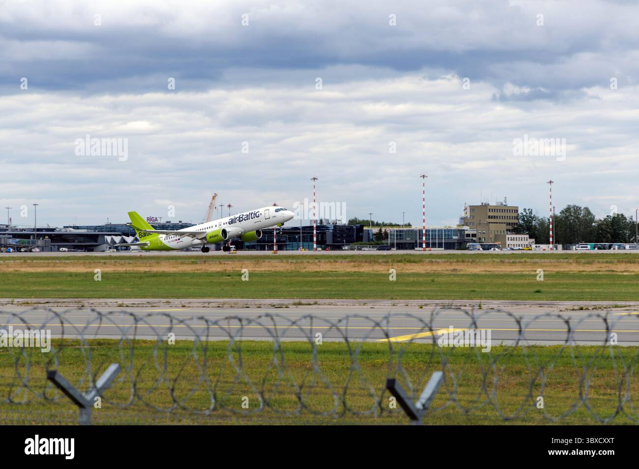 RIGA/LETTONIA – 07.06.2025: Un aeroplano Baltico decolla dall'aeroporto internazionale di riga, con hangar sullo sfondo, che simboleggiano la crescita di A. Foto Stock