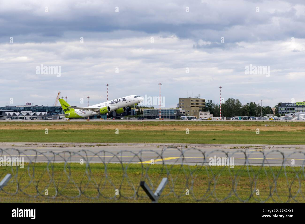 RIGA/LETTONIA – 07.06.2025: Un aeroplano Baltico decolla dall'aeroporto internazionale di riga, con hangar sullo sfondo, che simboleggiano la crescita di A. Foto Stock