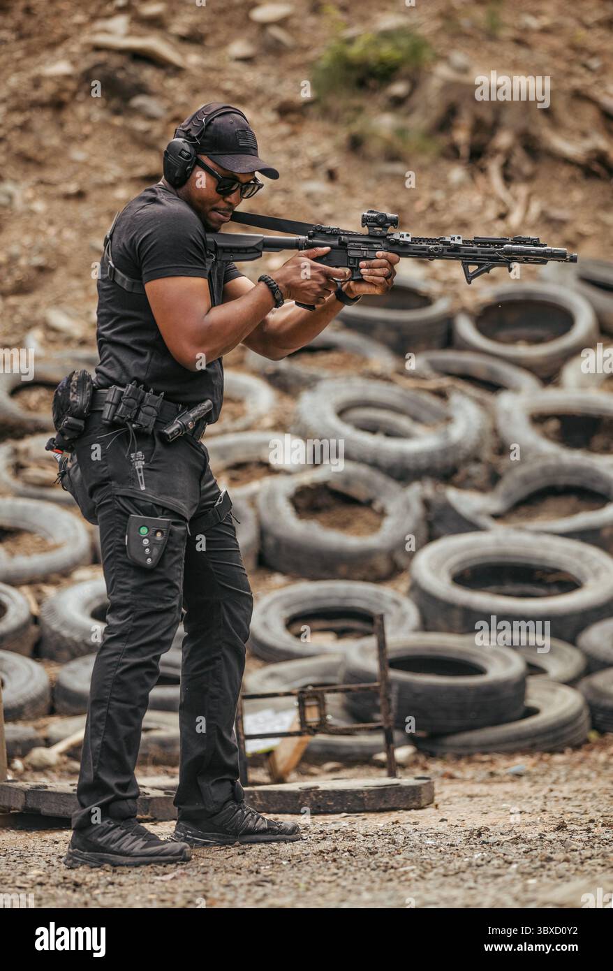 Un uomo con equipaggiamento tattico punta un fucile su un bersaglio durante la pratica del bersaglio Foto Stock