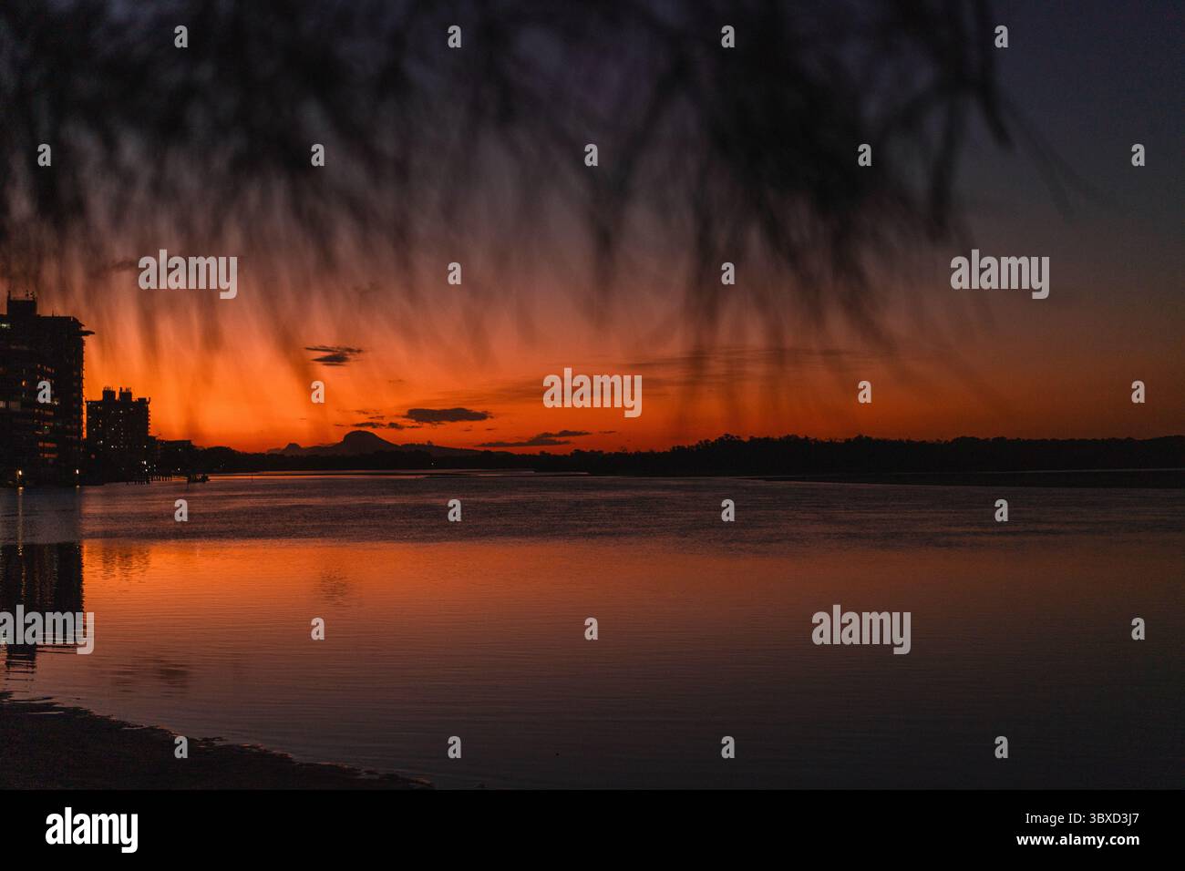 Silhouette dello skyline della città al tramonto con riflessi sull'acqua calma Foto Stock