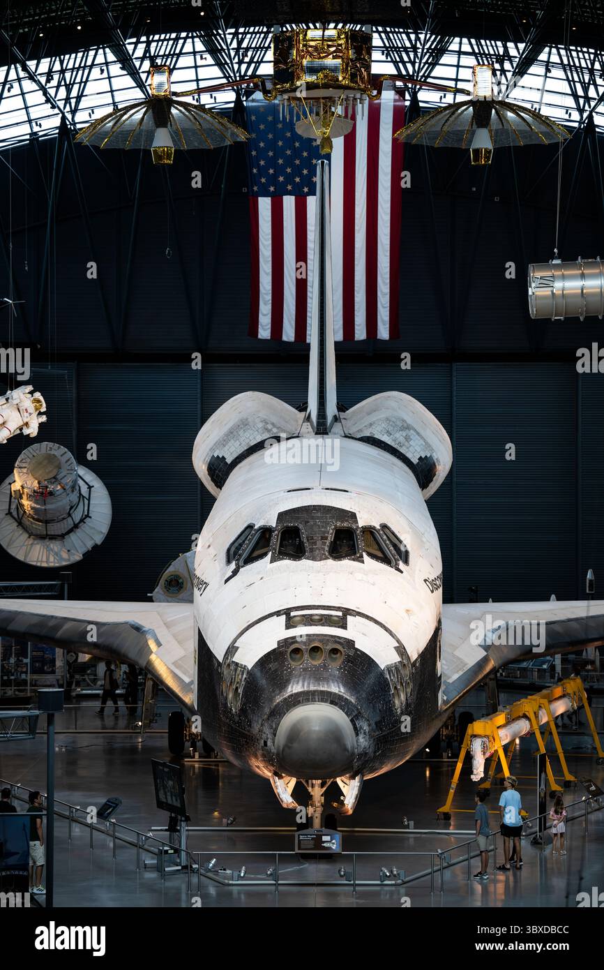 Space Shuttle Discovery display allo Steven F Udvar-Hazy Center a Chantilly Virginia | CHANTILLY, Virginia - i visitatori si riuniscono sotto la fusoliera e i propulsori di controllo della reazione in avanti della Discovery allo Steven F. Udvar-Hazy Center, dove l'orbiter in pensione è sospeso vicino a una navicella Gemini e a una tuta da astronauta. Discovery è stato designato dalla NASA come "veicolo di registrazione", mantenuto in gran parte non restaurato in modo che gli ingegneri potessero studiare un vero orbiter volato. È esposto qui dall'aprile 2012. Foto Stock
