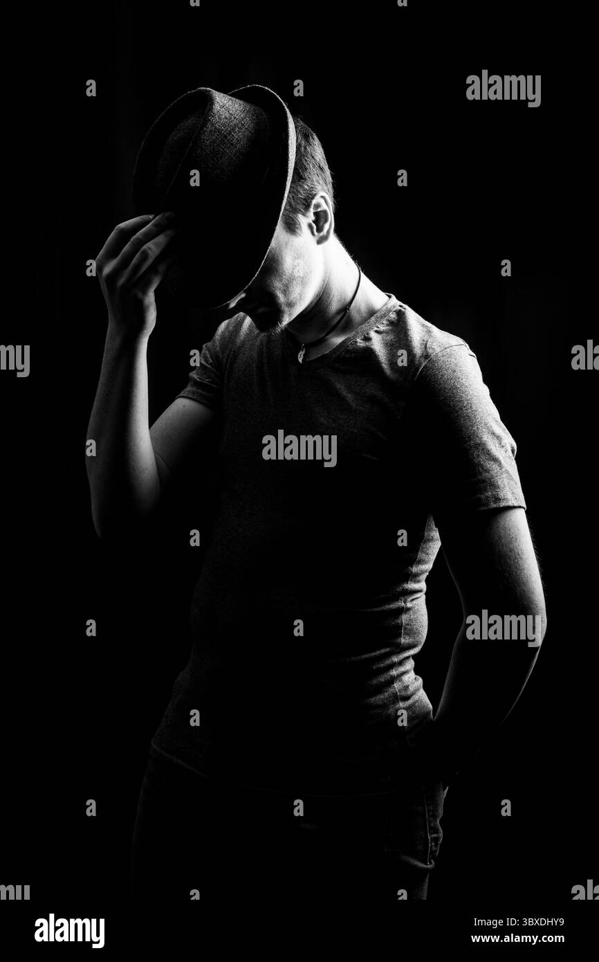 Un avvincente ritratto in bianco e nero di un uomo, parzialmente oscurato dall'ombra, che rovescia rispettosamente la sua fedora. Foto Stock