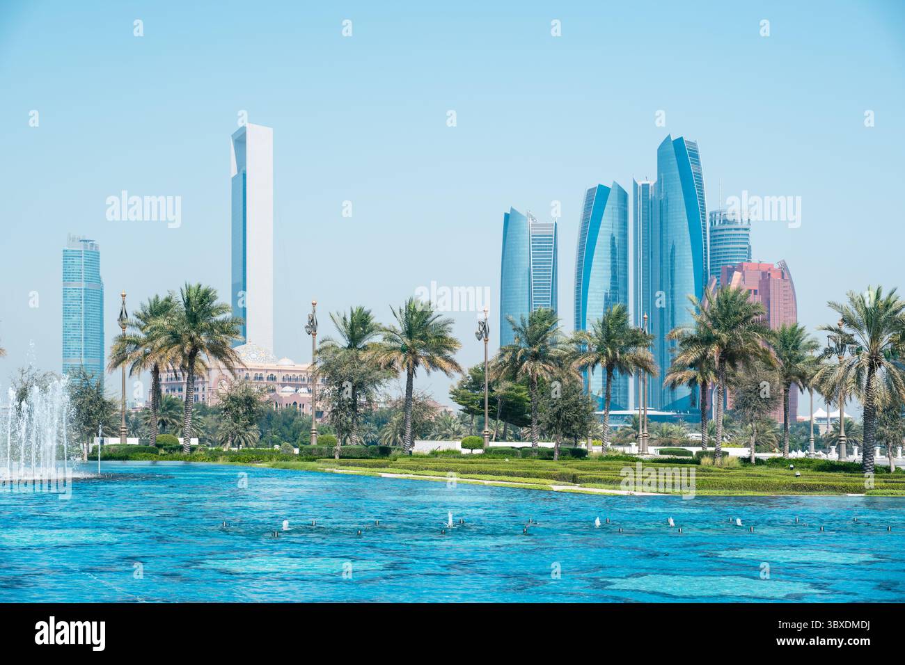 Skyline di Abu Dhabi con grattacieli alti e moderni, palme e una fontana in primo piano sotto il cielo azzurro Foto Stock