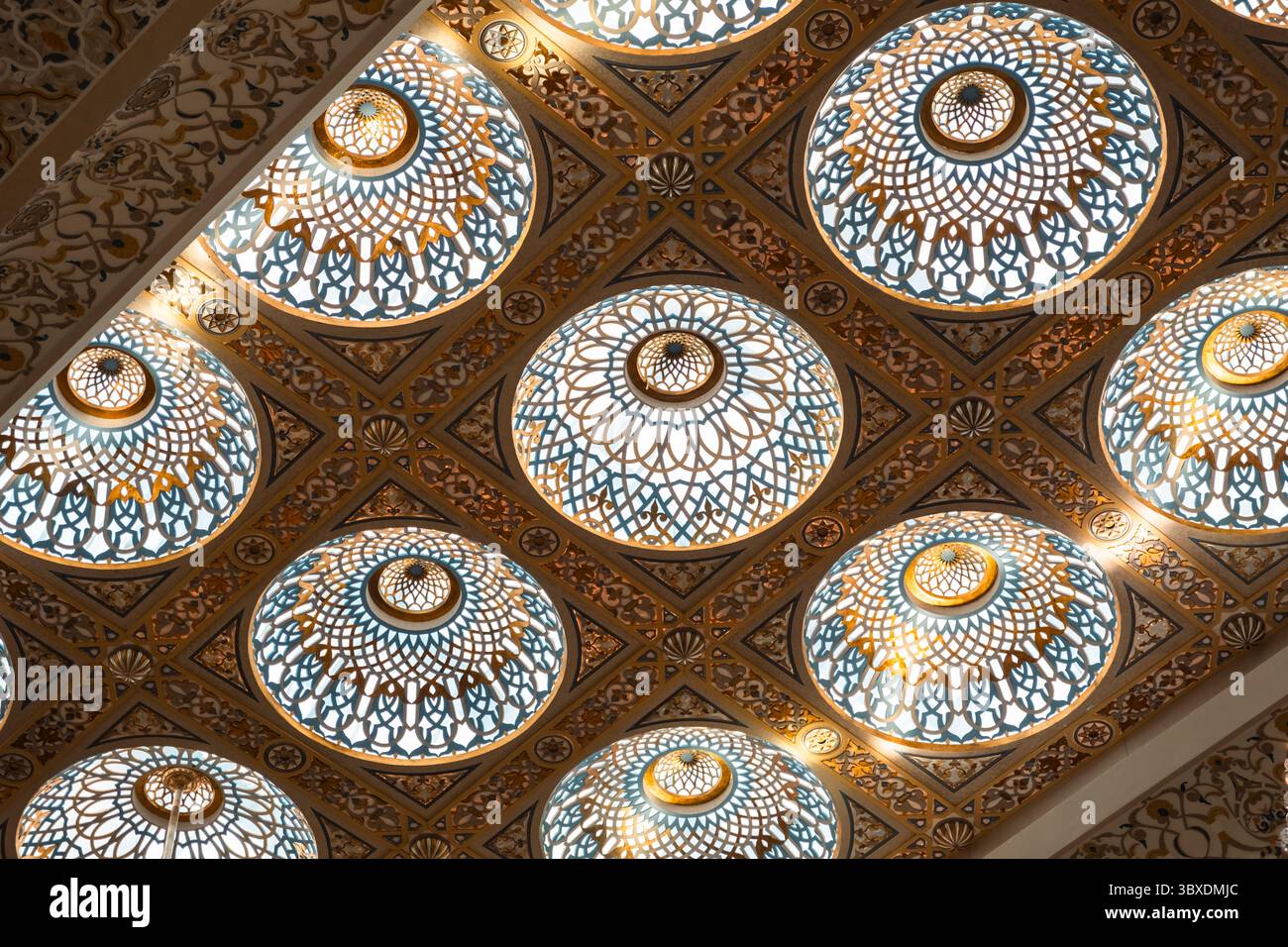 soffitti interni lussuosi e dettagliati con intricati motivi geometrici e vetrate colorate circolari, illuminate dalla luce, che creano una simmetrica Foto Stock