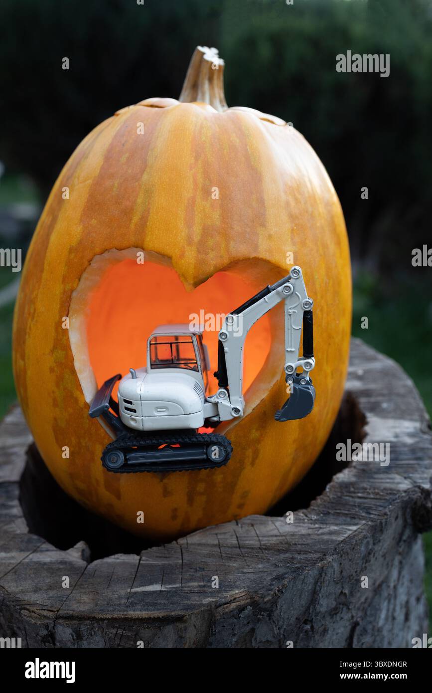 Modello giocattolo in metallo di escavatore con cuore di zucca arancione. Concetto di business dei saluti del Ringraziamento per le imprese di costruzione. Cartolina Foto Stock