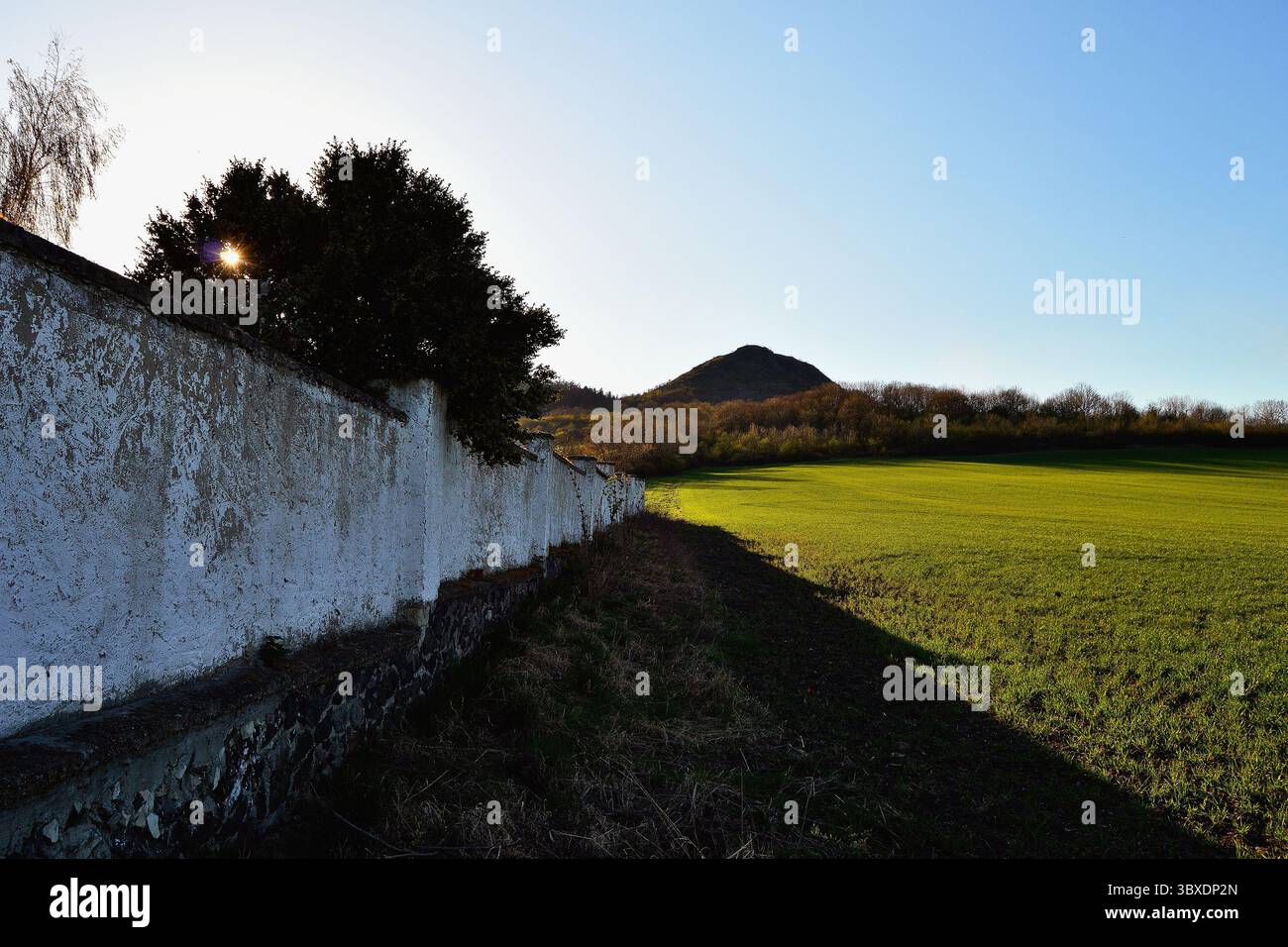 Sunlit Hill con Green Fields e White Wall Casting Sharp Shadow Foto Stock