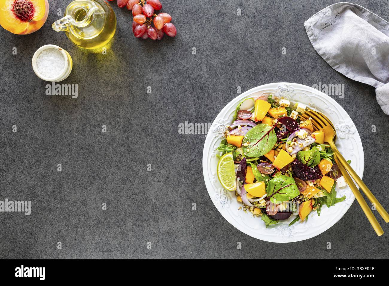 Cibo, insalata di verdure fresche con barbabietole, rucola, cipolla rossa, sorrel, ceci, pesca e uva in un piatto bianco su sfondo nero Foto Stock