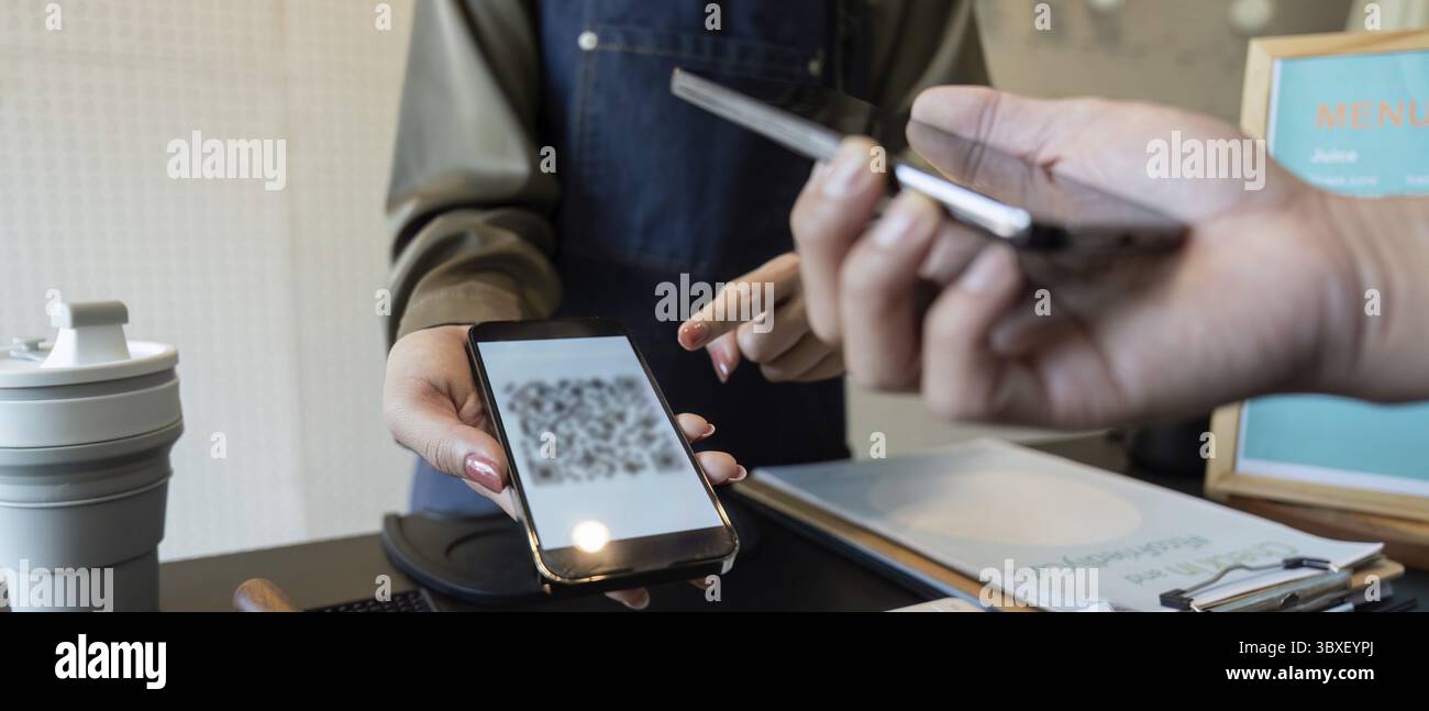 Un barista e un cliente si impegnano in una transazione di pagamento contactless, sottolineando la praticità e supportando pratiche sostenibili Foto Stock