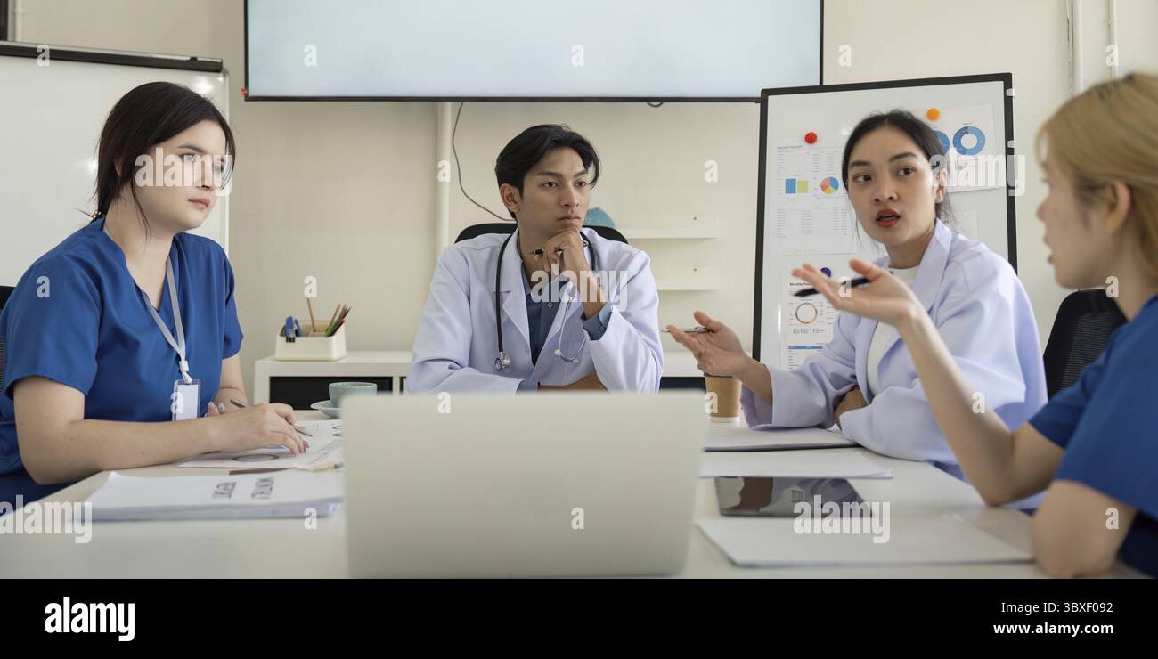 Un gruppo eterogeneo di professionisti del settore sanitario che discutono attivamente le strategie di assistenza ai pazienti e analizzano i dati durante una riunione di gruppo in un ufficio moderno Foto Stock