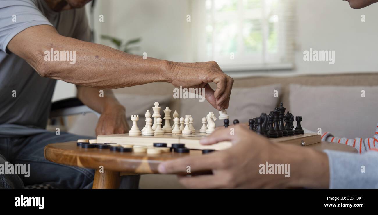 Una vista ravvicinata di un padre che fa abilmente una mossa scacchistica mentre suo figlio osserva attentamente, mostrando il loro legame familiare attraverso interessi condivisi Foto Stock