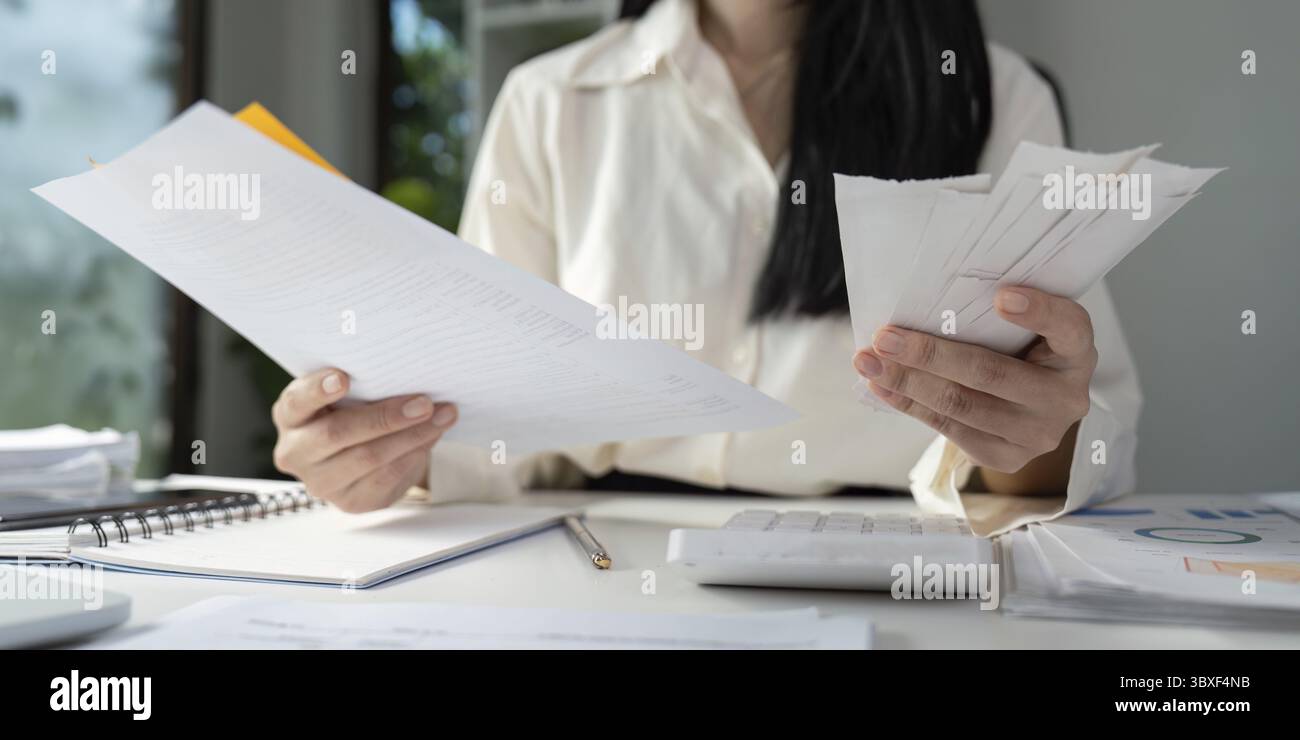 Una persona detiene moduli fiscali e rivede documenti finanziari, concentrandosi sull'importanza della preparazione fiscale Foto Stock