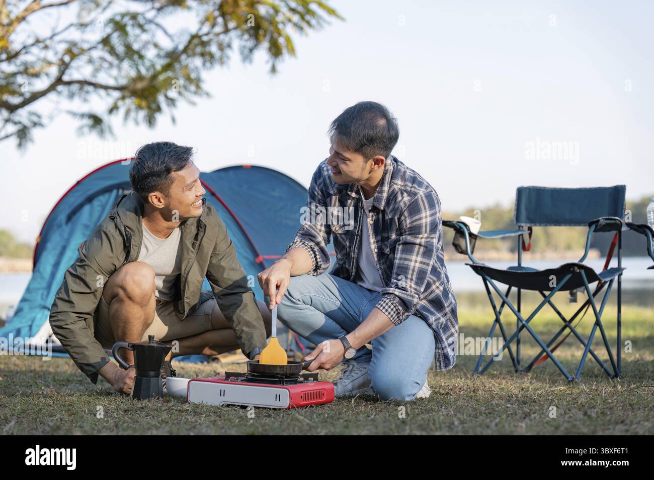 Una felice coppia gay che cammina all'aperto e prepara la colazione accanto alla tenda. Amano la natura e trascorrono del tempo insieme Foto Stock