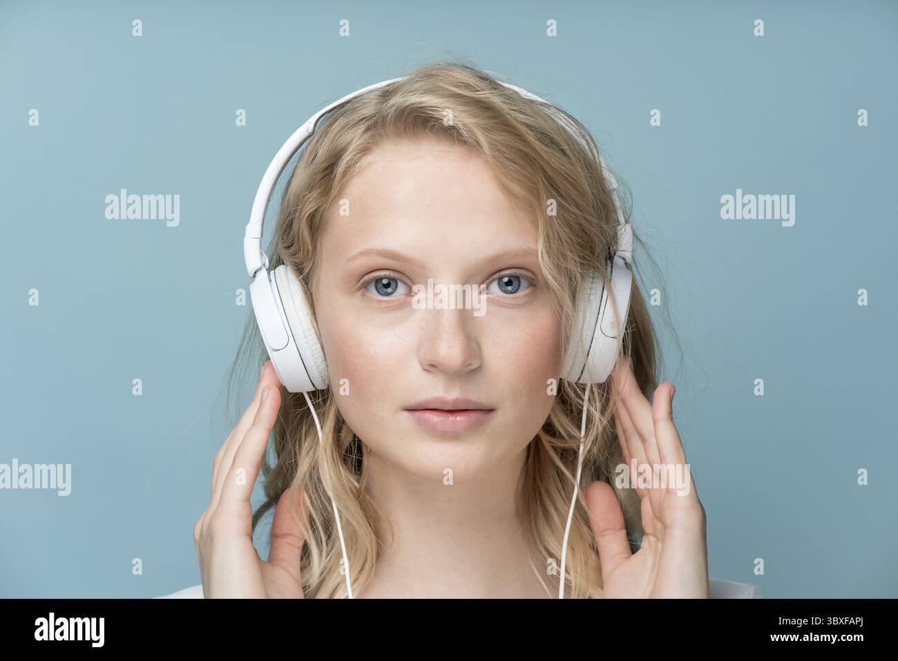 Ritratto ravvicinato di una giovane donna ad occhi chiusi che ascolta musica tramite le cuffie sul muro Aqua Menthe con tonalità neutra a colori. Una donna bionda molto seria e intelligente Foto Stock