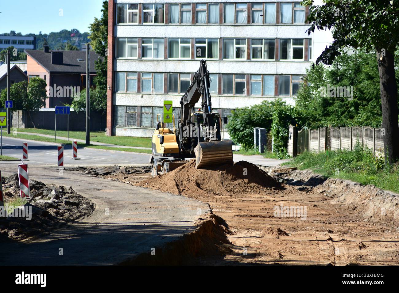 Escavatore in fase di costruzione di strade urbane durante l'estate. L'attrezzatura di movimento terra prepara la base per la nuova strada come guida per i veicoli. INF Foto Stock