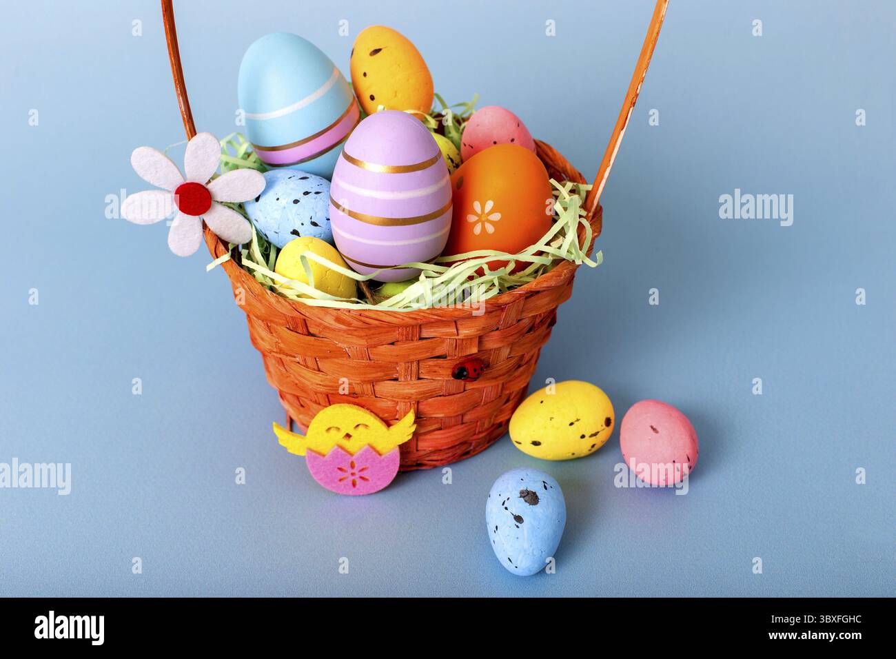 Primo piano del cestino di vimini riempito di uova decorative multicolore su sfondo azzurro Foto Stock