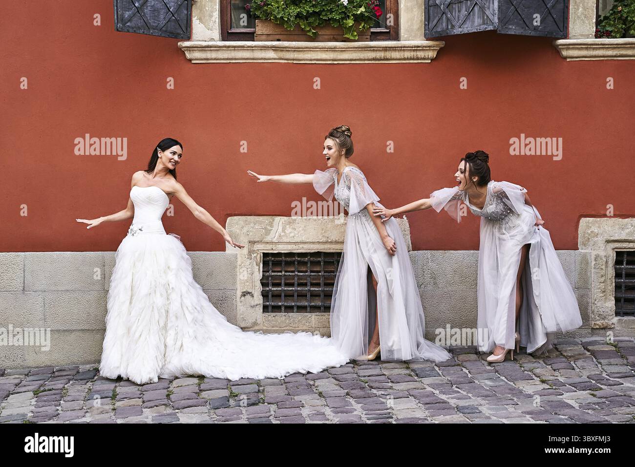 Bella sposa e bridesmaids in splendidi abiti argentati luce in vecchia bella città europea in un giorno di nozze in estate. Gli abiti sono lunghezza pavimento o Foto Stock