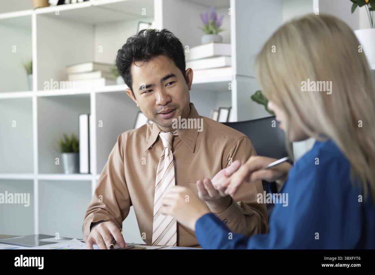 Un contabile e un'analista finanziaria maschile impegnati in una discussione strategica, condividendo informazioni sulle metriche aziendali in un ufficio contemporaneo Foto Stock