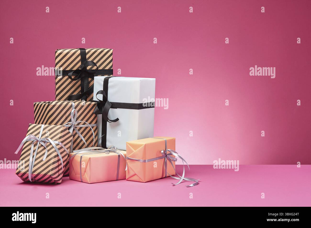 Dimensioni differenti, colorati a strisce e pianura, marrone, rosa e bianco presente carta scatole legate con nastri multicolori e archi su una superficie di colore rosa e Foto Stock