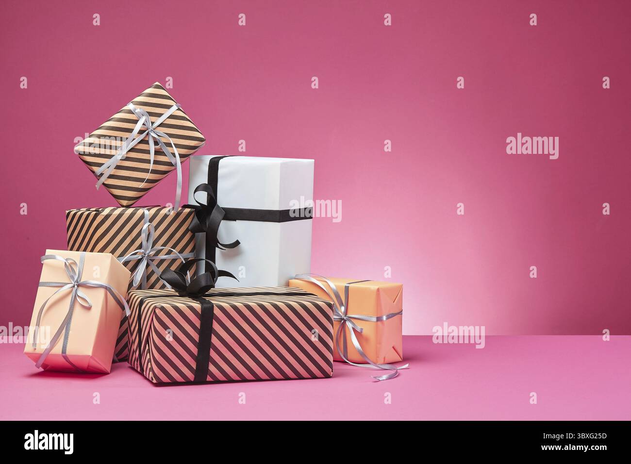 Dimensioni differenti, colorati a strisce e pianura, marrone, rosa e bianco carta scatole regalo legato con nastri multicolori e archi su una superficie di colore rosa e Foto Stock
