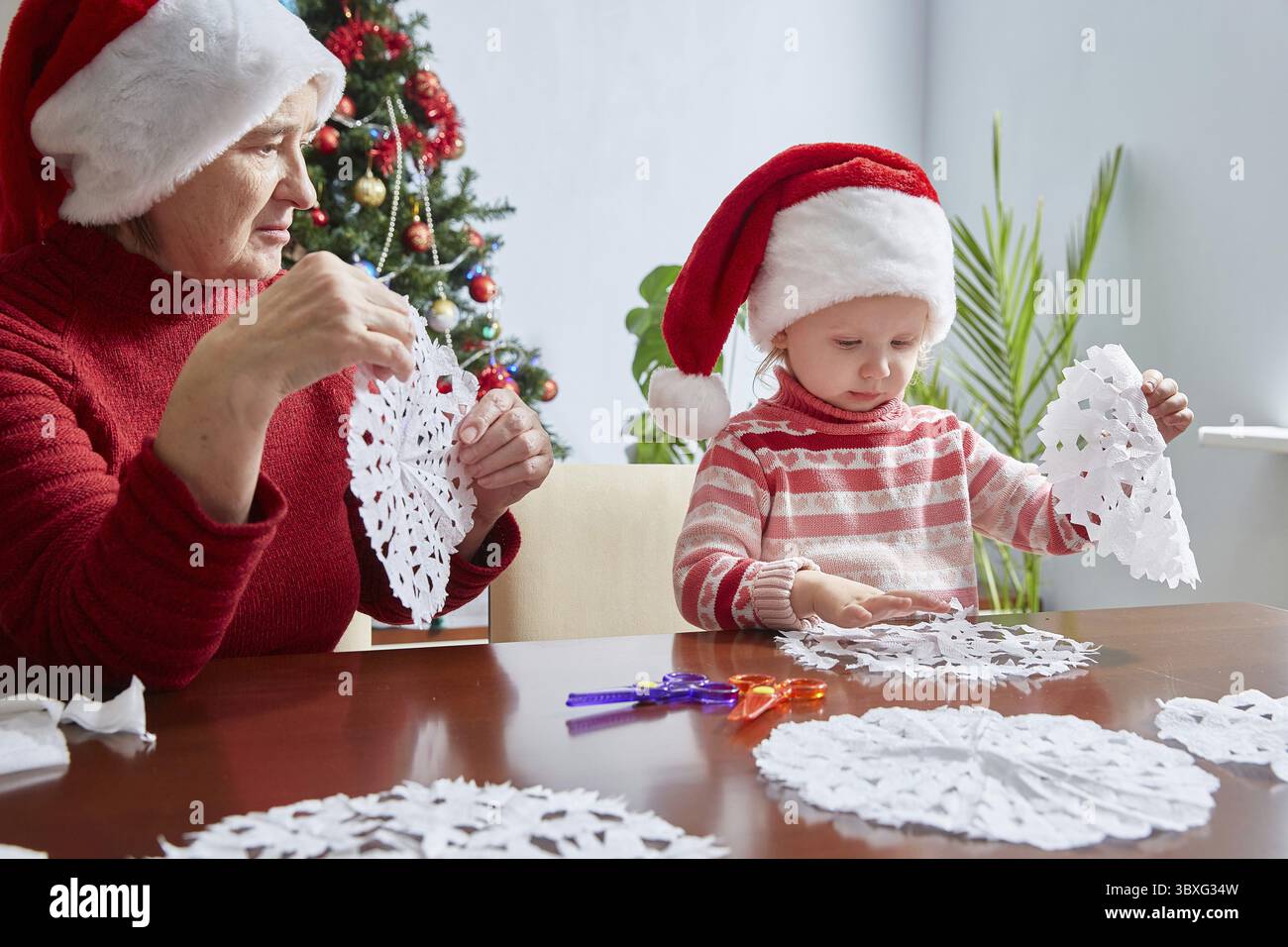 Tradizioni di famiglia. Decorazioni per la casa per Capodanno e Natale. Nonna e nipote fanno fiocchi di neve dalla carta Foto Stock
