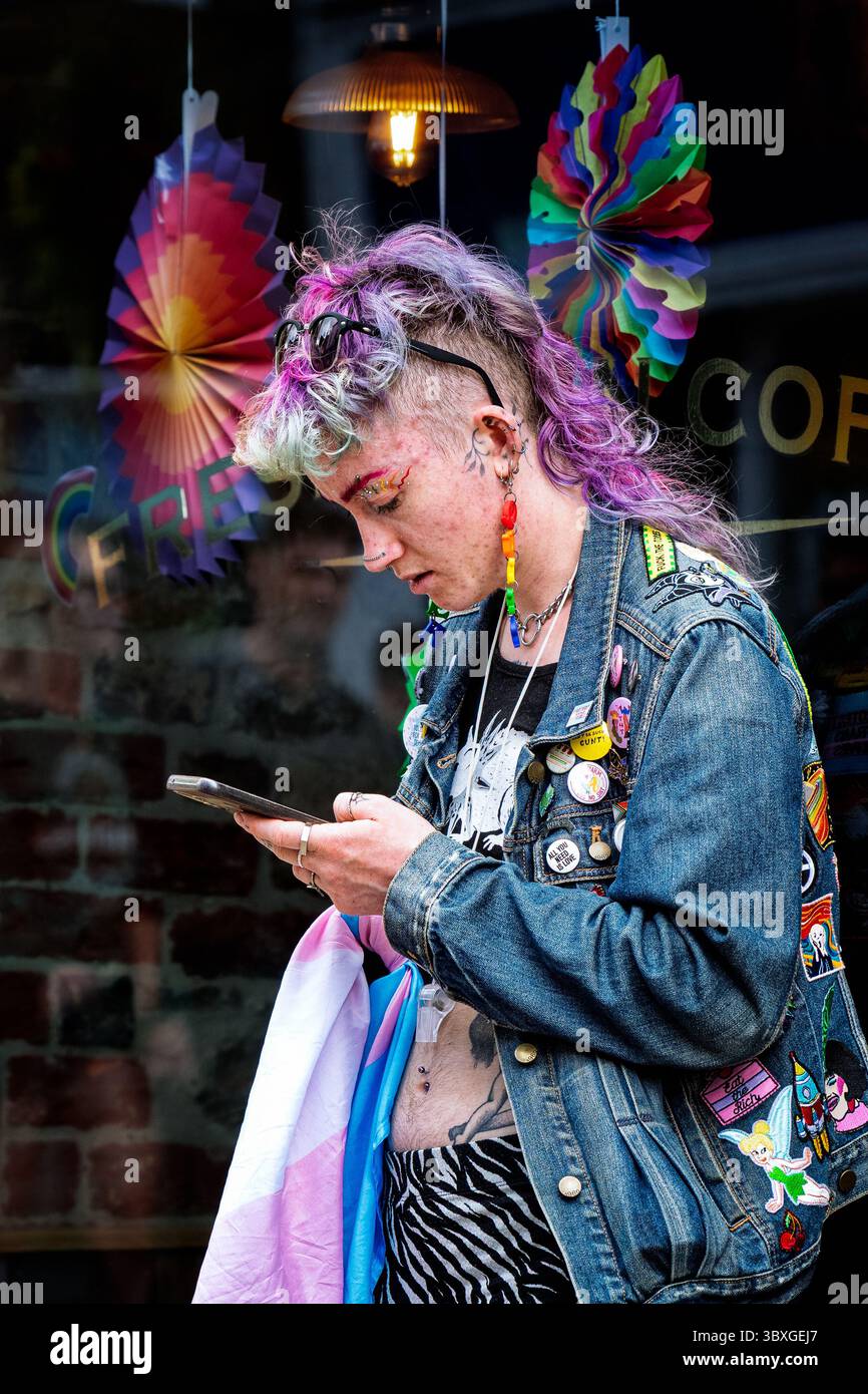 Durante lo Sherborne Pride nel Dorset, un partecipante vivace con un'acconciatura unica controlla il proprio telefono. Foto Stock