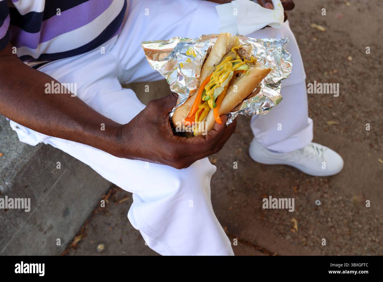 Un uomo di colore che mangia una salsiccia bratwurst Foto Stock