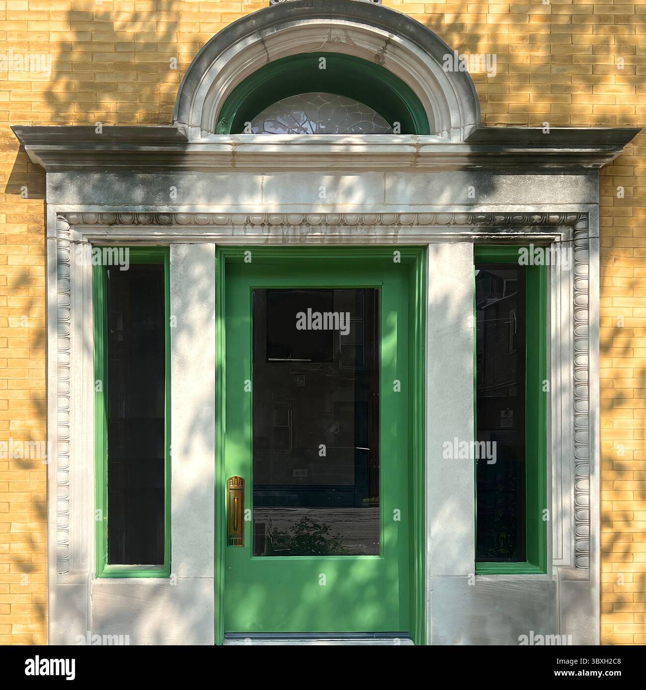 Porta verde lime con luci di posizione e specchio di poppa ad arco incorniciato da dettagli in pietra scolpita su una facciata in mattoni gialli a Chicago, abbellita dall'ombra mattutina. Foto Stock