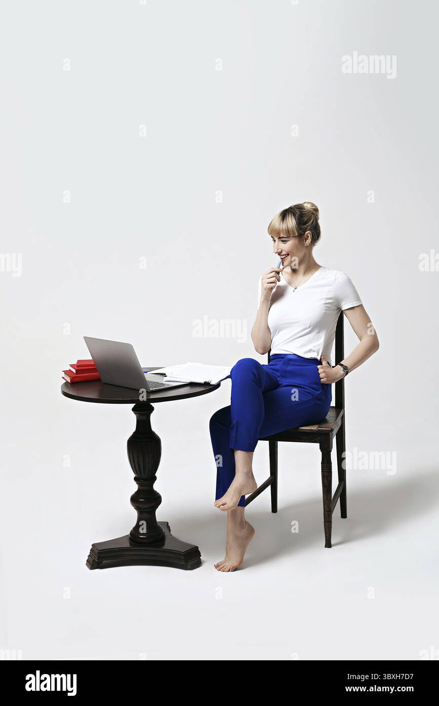 Giovane donna concentrata seduto alla scrivania che lavora o studia a distanza scrivendo note mentre si guarda sullo schermo del notebook. Apprendimento a distanza o remoto Foto Stock