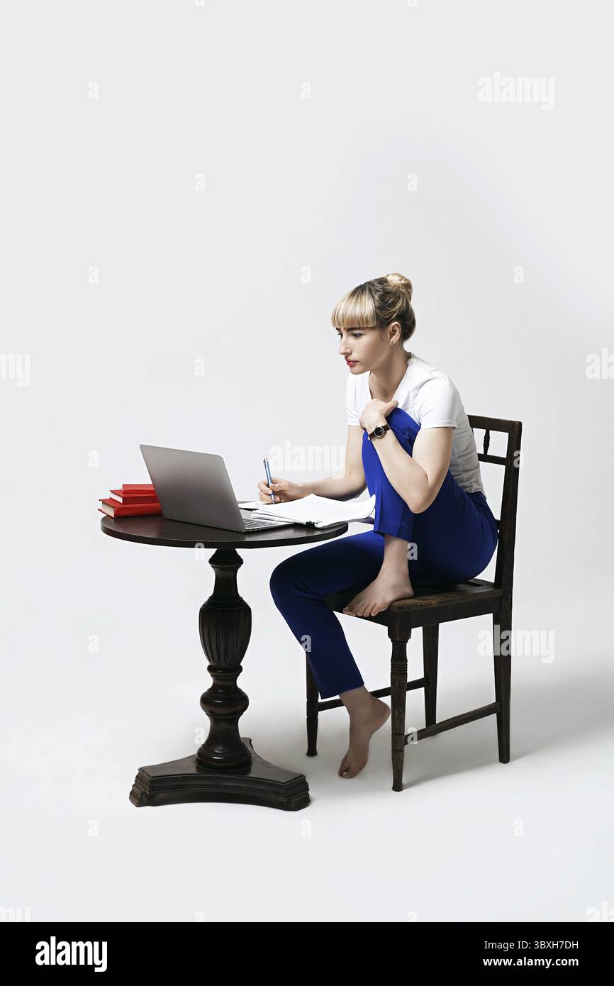 Giovane studentessa concentrata che lavora alla scrivania o studia in remoto online scrivendo appunti mentre guarda sullo schermo del notebook. Apprendimento a distanza o rem Foto Stock