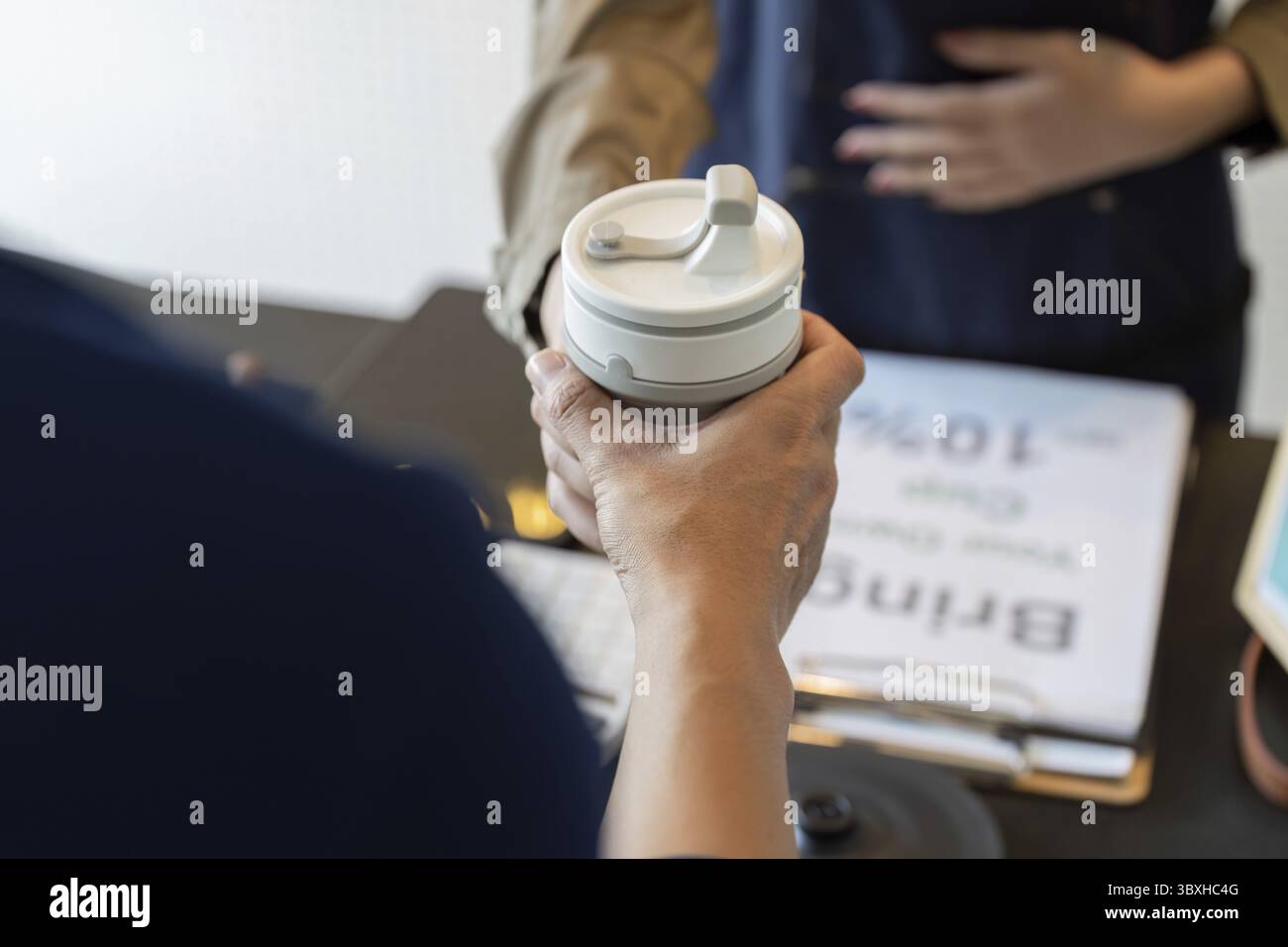 Il cliente offre la tazza riutilizzabile al barista, partecipando all'iniziativa caffè per ridurre gli sprechi e promuovere la sostenibilità Foto Stock