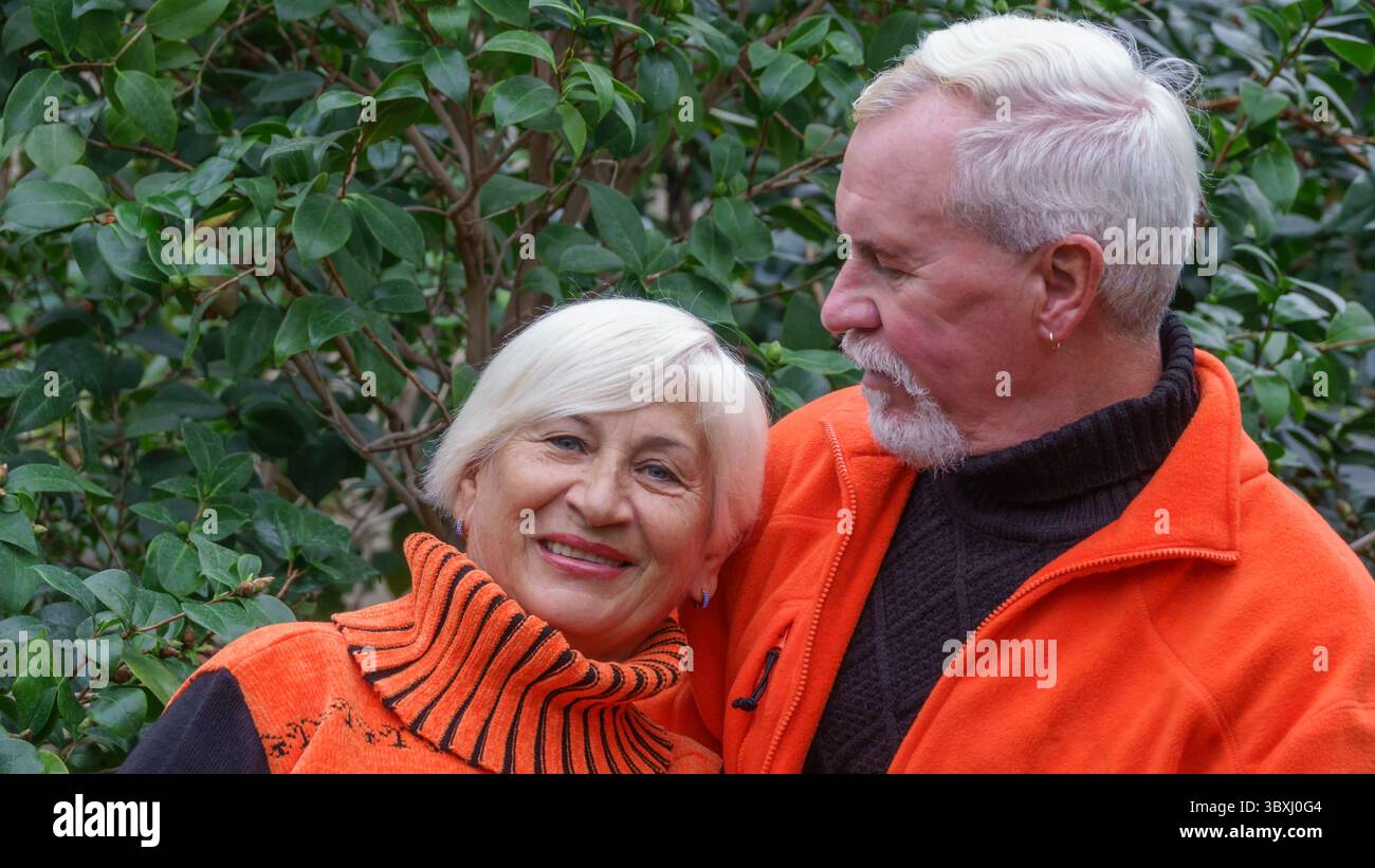 Felice anziani bella coppia sposata con i capelli grigi in arancione sportswear contro uno sfondo di serra piante esotiche Foto Stock