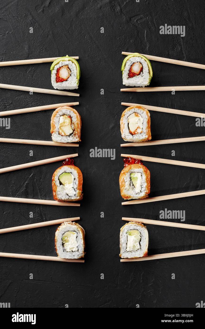 Vari appetitosi sushi Rolls con salmone, anguilla, gamberi, avocado e caviale in bacchette su superficie ruvida nera, vista dall'alto. Concetto di popolarità o Foto Stock