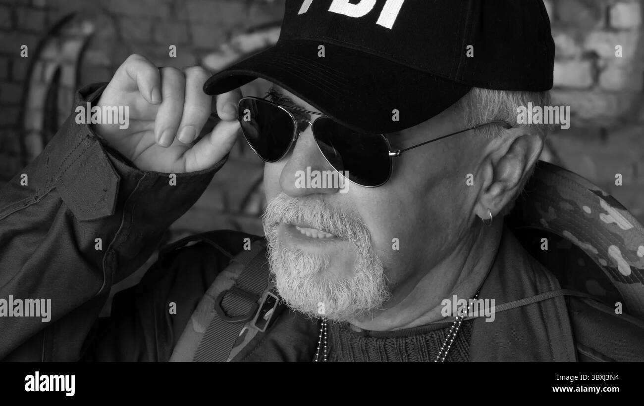 Ritratto di fiducioso uomo anziano indossare abbigliamento protettivo in occhiali da sole contro lo sfondo di vecchi muri di cemento Foto Stock