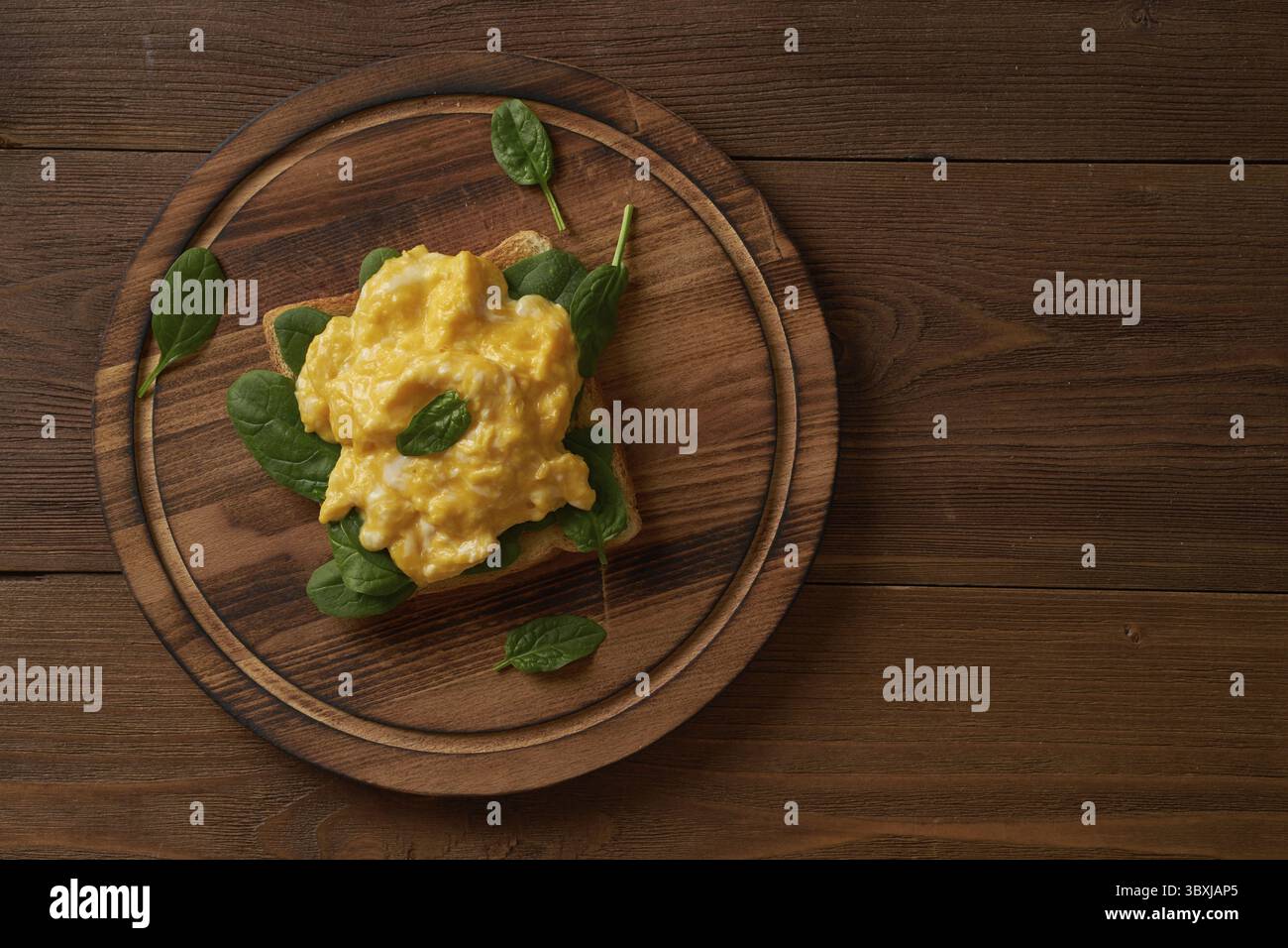 Toast con uova strapazzate e spinaci. Omelette. Colazione con uova fritte su sfondo marrone scuro. Vista dall'alto Foto Stock