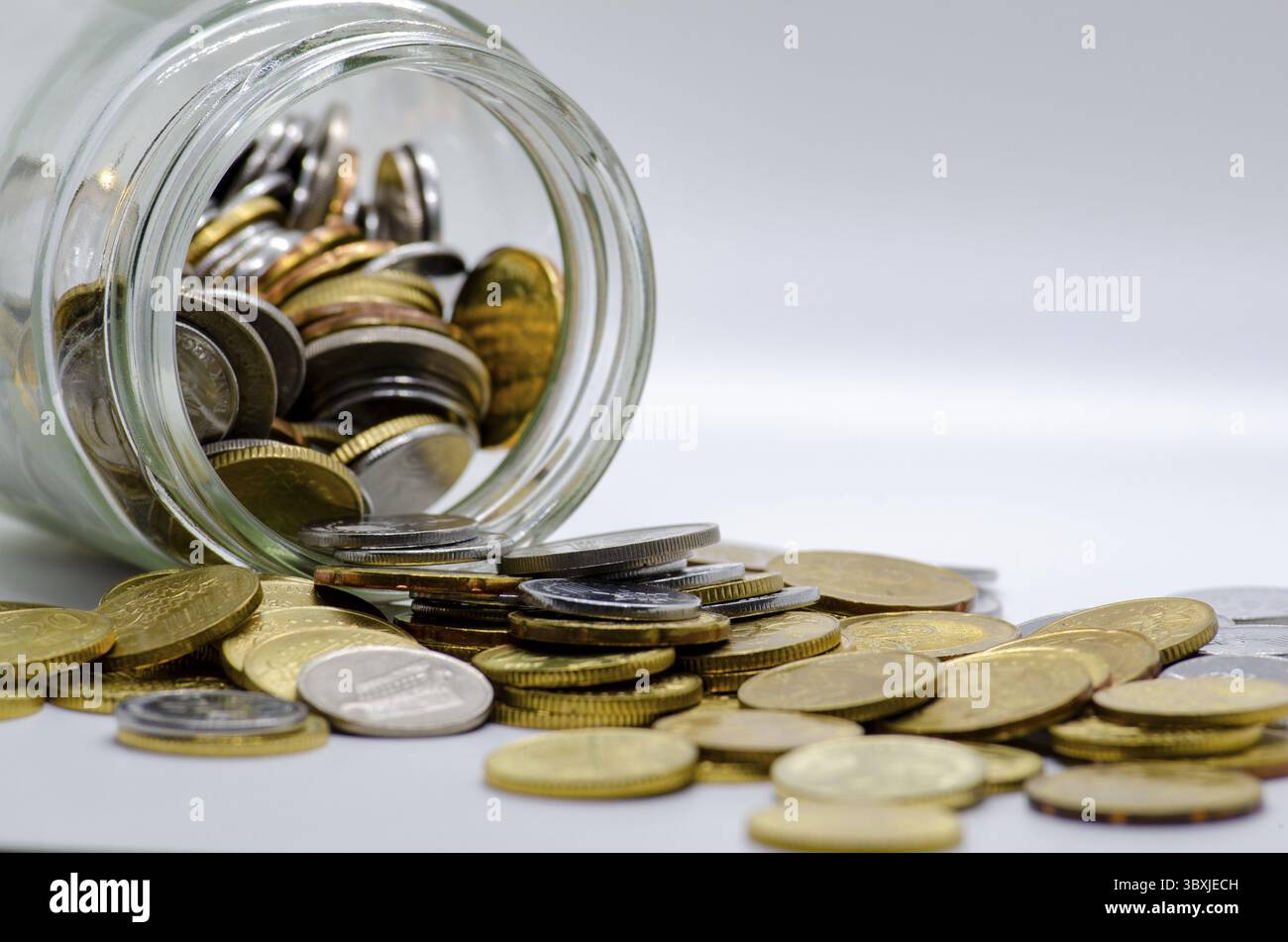 Monete in vaso con sfondo bianco che rappresentano attività, investimenti o qualsiasi concetto monetario. Spazio personalizzabile per il testo Foto Stock