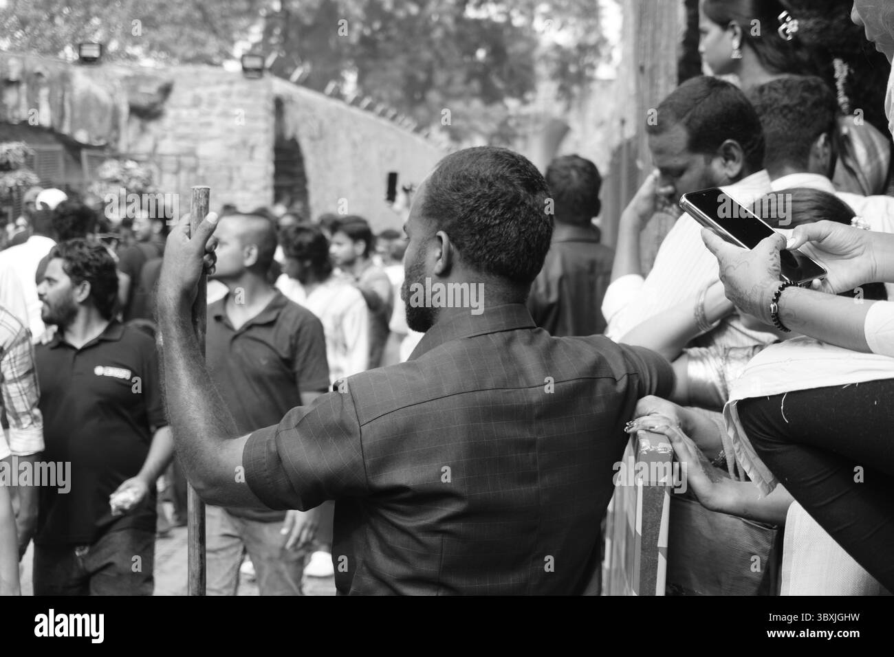 Guardia di sicurezza che riposa le mani sul bastone in mezzo a una folla Foto Stock