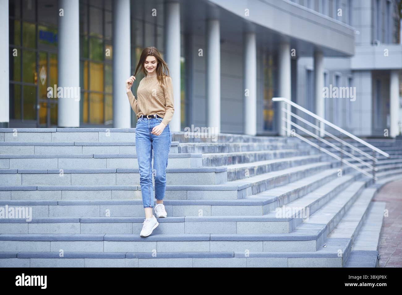 Una giovane donna cammina lungo i gradini di un edificio grigio in una fredda giornata estiva o in un caldo autunno Foto Stock
