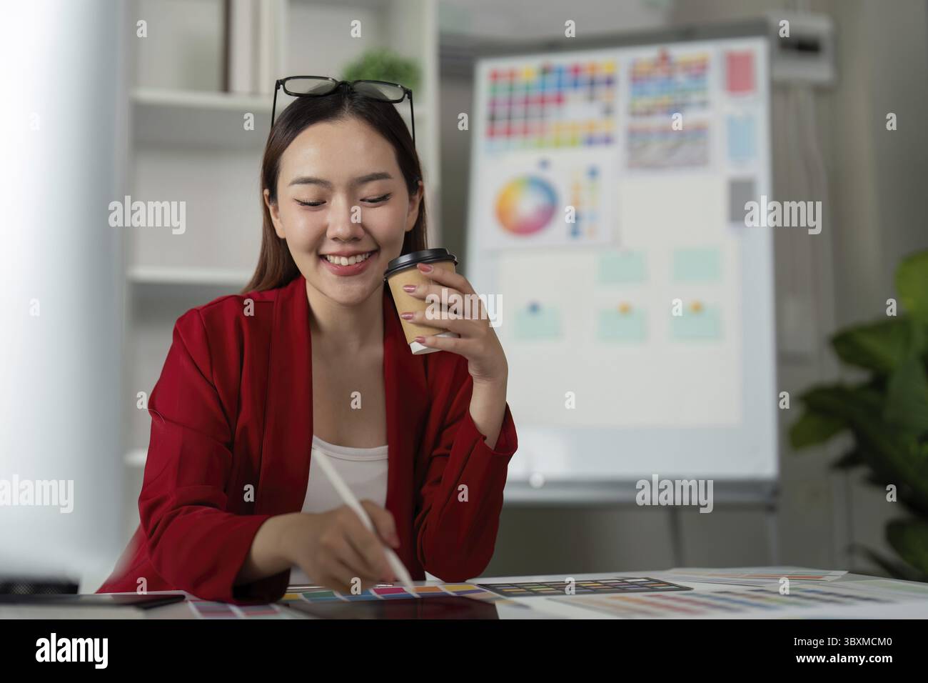 Mettendo in risalto il suo stile creativo, una designer bilancia relax e produttività, disegnando idee vivaci sul suo tablet mentre sorseggia un caffè Foto Stock