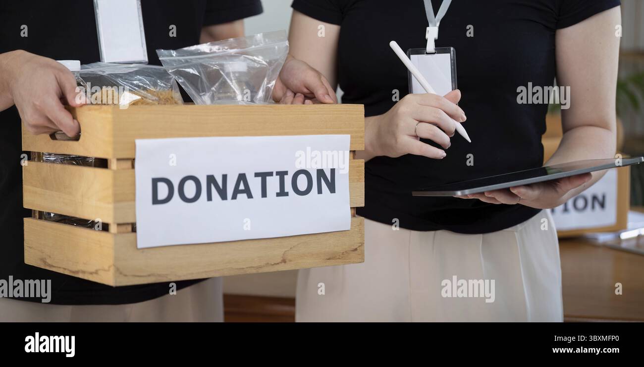 Volontari che utilizzano un tablet per registrare e gestire i beni donati durante un evento di beneficenza, evidenziando le competenze organizzative e il lavoro di squadra Foto Stock