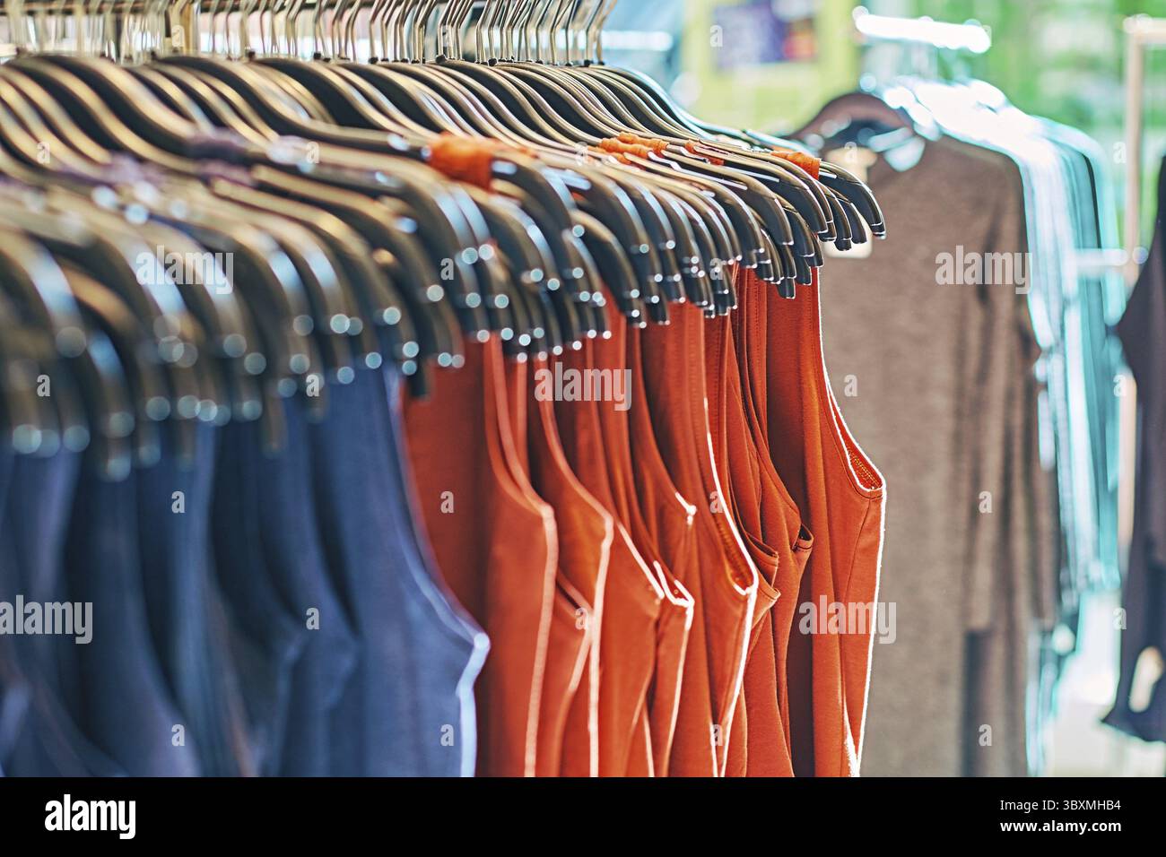Interno del negozio di abbigliamento alla moda con abiti da donna diversi su appendiabiti in rosso, blu e altri colori Foto Stock