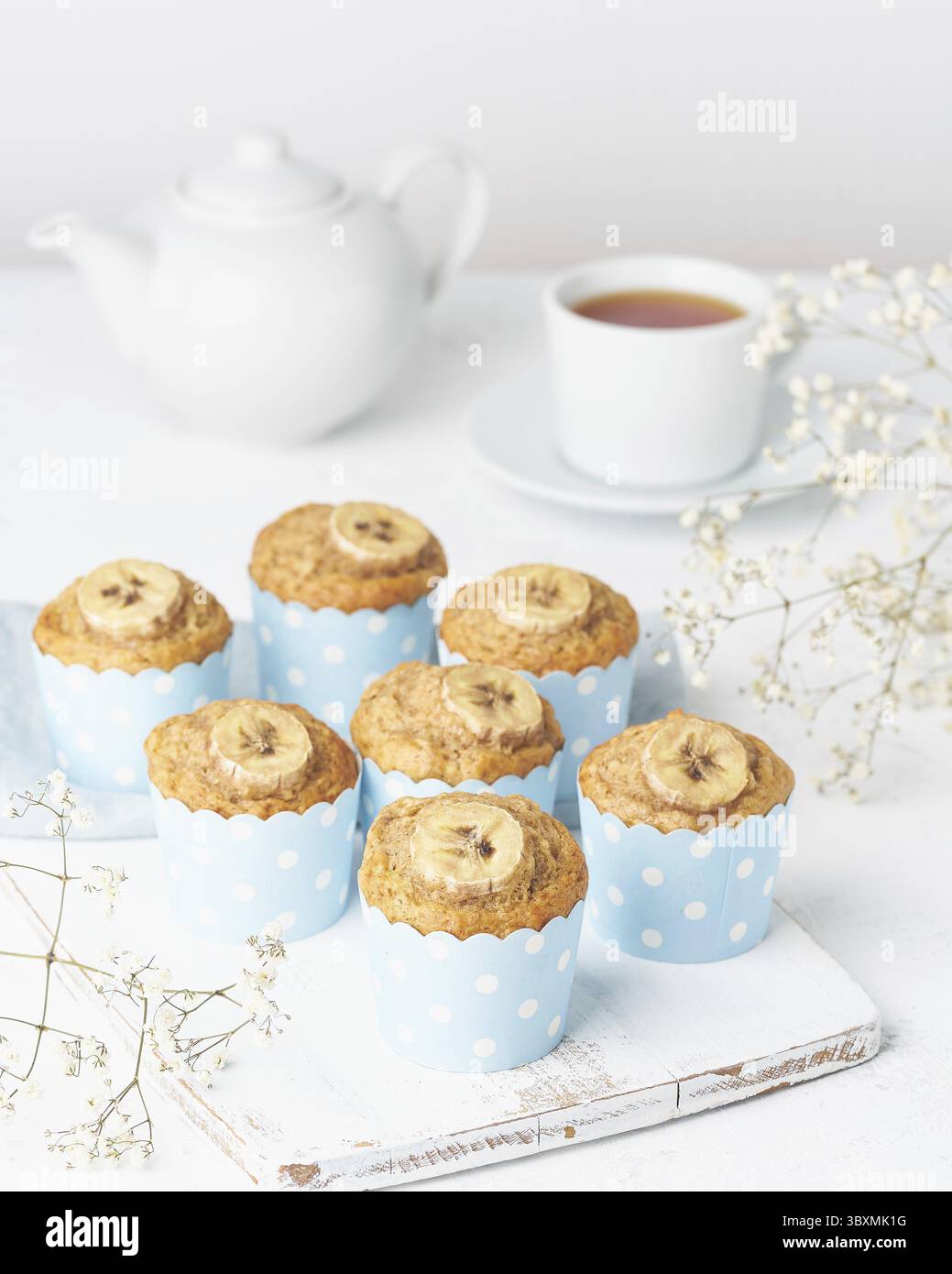 Muffin alla banana, cupcakes in una carta blu per torte, vista laterale, verticale, tavola bianca in cemento Foto Stock