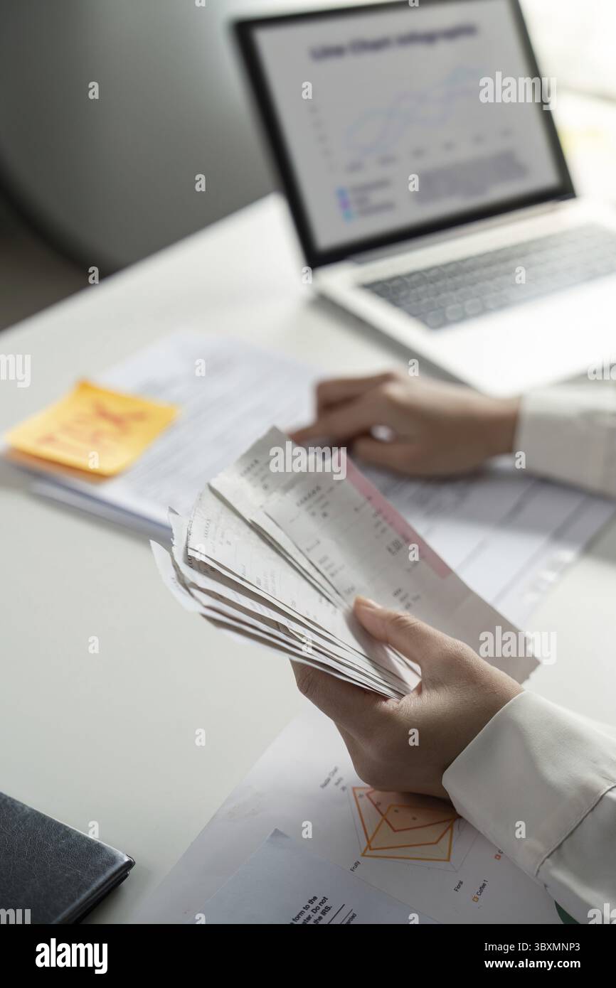 Una persona esamina le informazioni finanziarie su uno smartphone mentre gestisce la documentazione fiscale, evidenziando il multitasking nella finanza Foto Stock