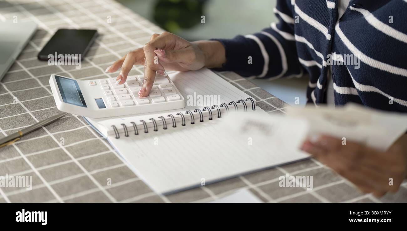 Una giovane donna concentrata utilizza una calcolatrice per gestire le proprie finanze e le proprie bollette, evidenziando l'importanza del budget e dell'alfabetizzazione finanziaria Foto Stock