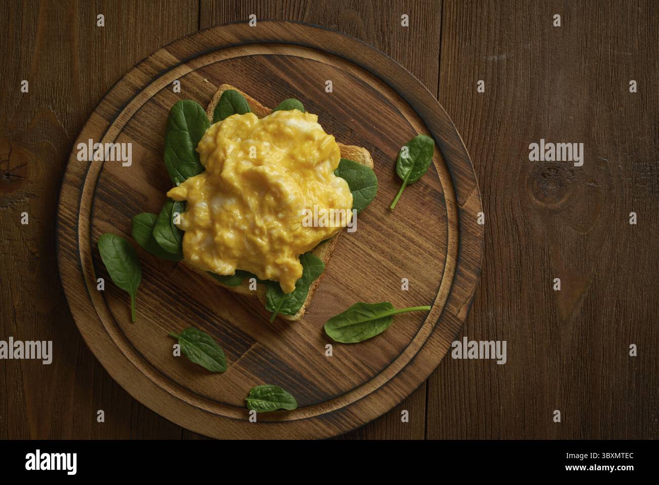 Toast con uova strapazzate e spinaci. Omelette. Colazione con uova fritte su sfondo marrone scuro. Vista dall'alto Foto Stock