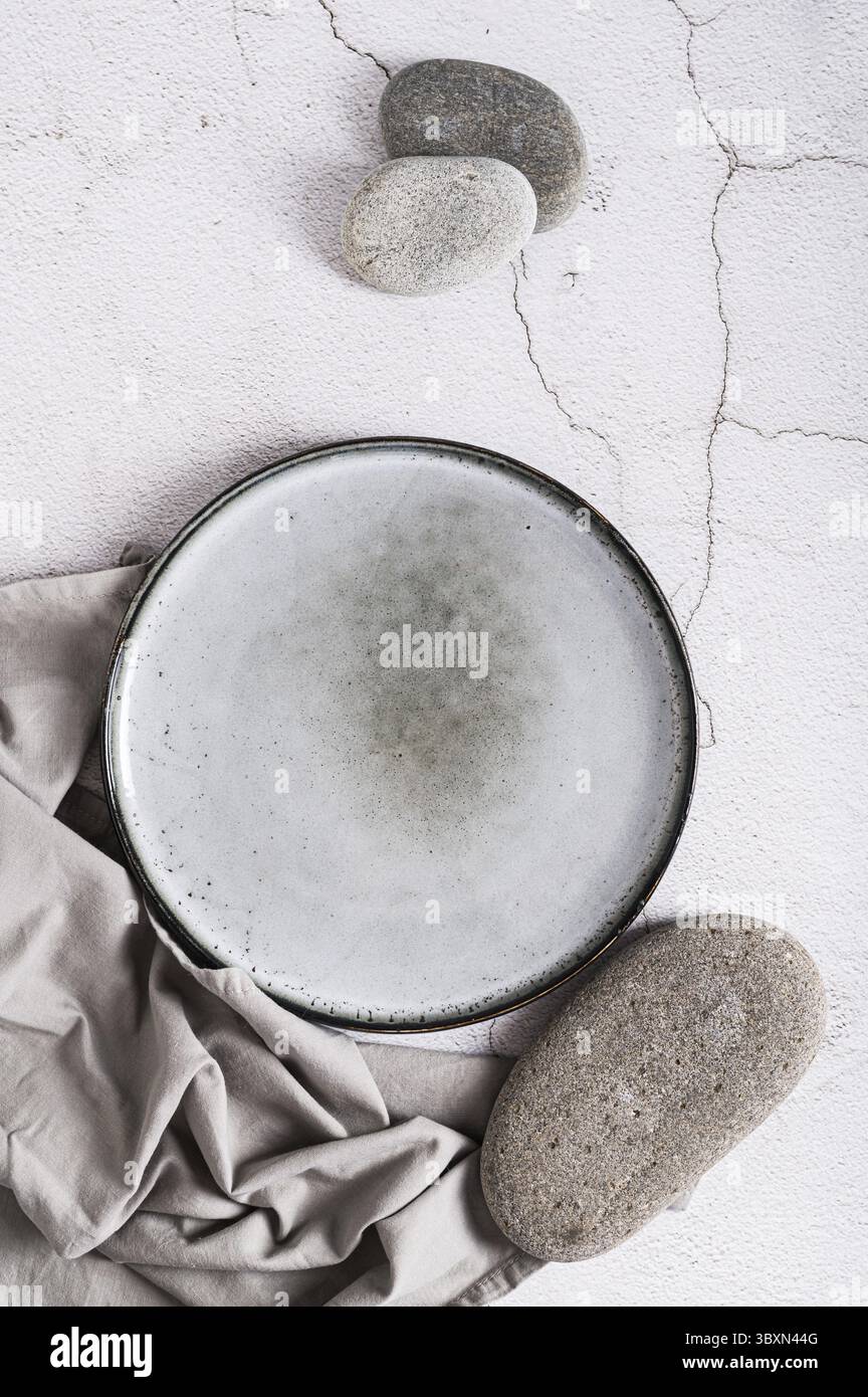 Cibo, piastra in ceramica vuota, pietre e tovagliolo su sfondo grigio dall'alto e vista verticale Foto Stock
