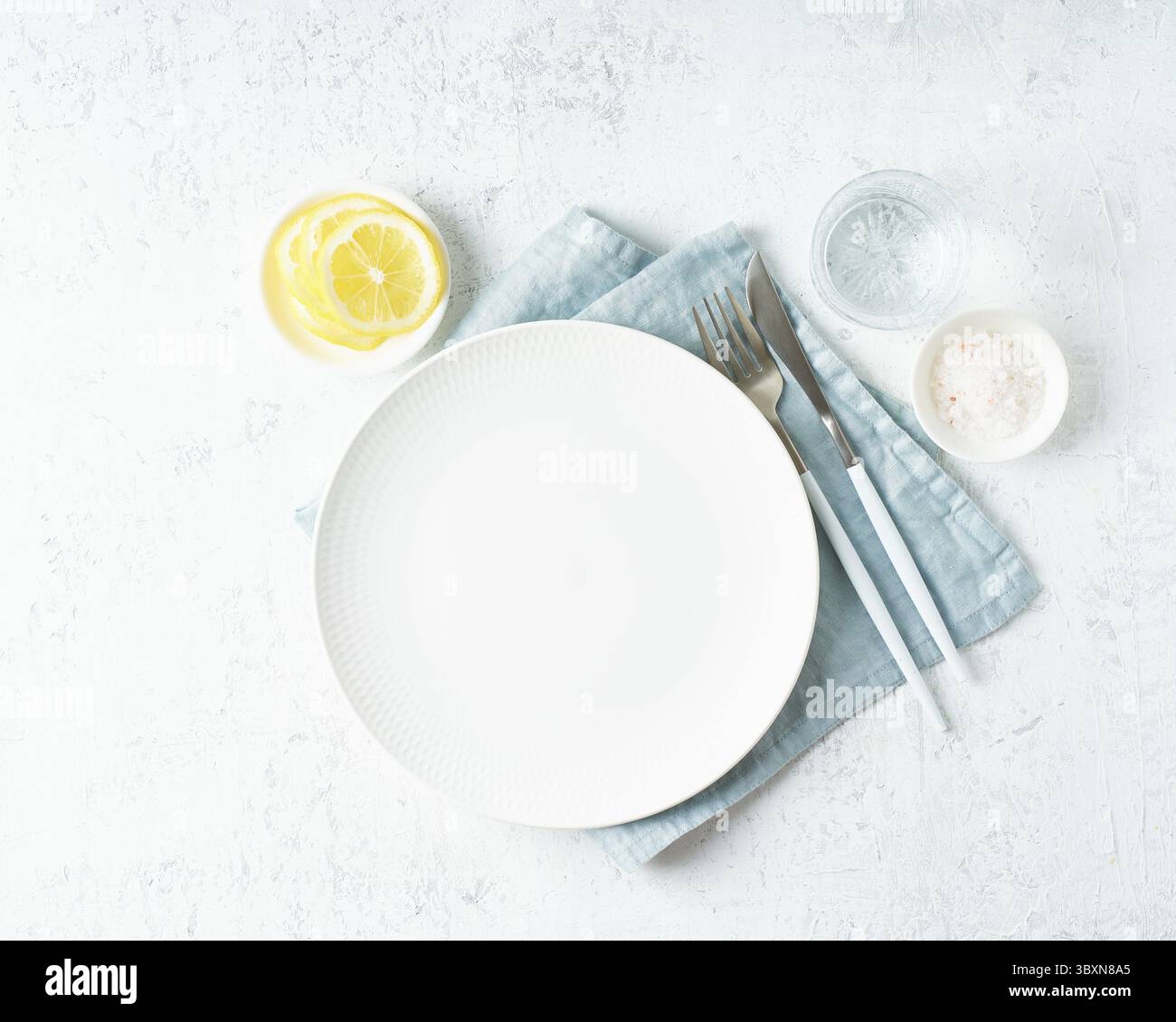 Pulire la piastra bianca vuota, il bicchiere d'acqua, la forchetta e il coltello sul tavolo in pietra bianca, lo spazio per le copie, il mock up, la vista dall'alto. Concetto di menu con utensile Foto Stock