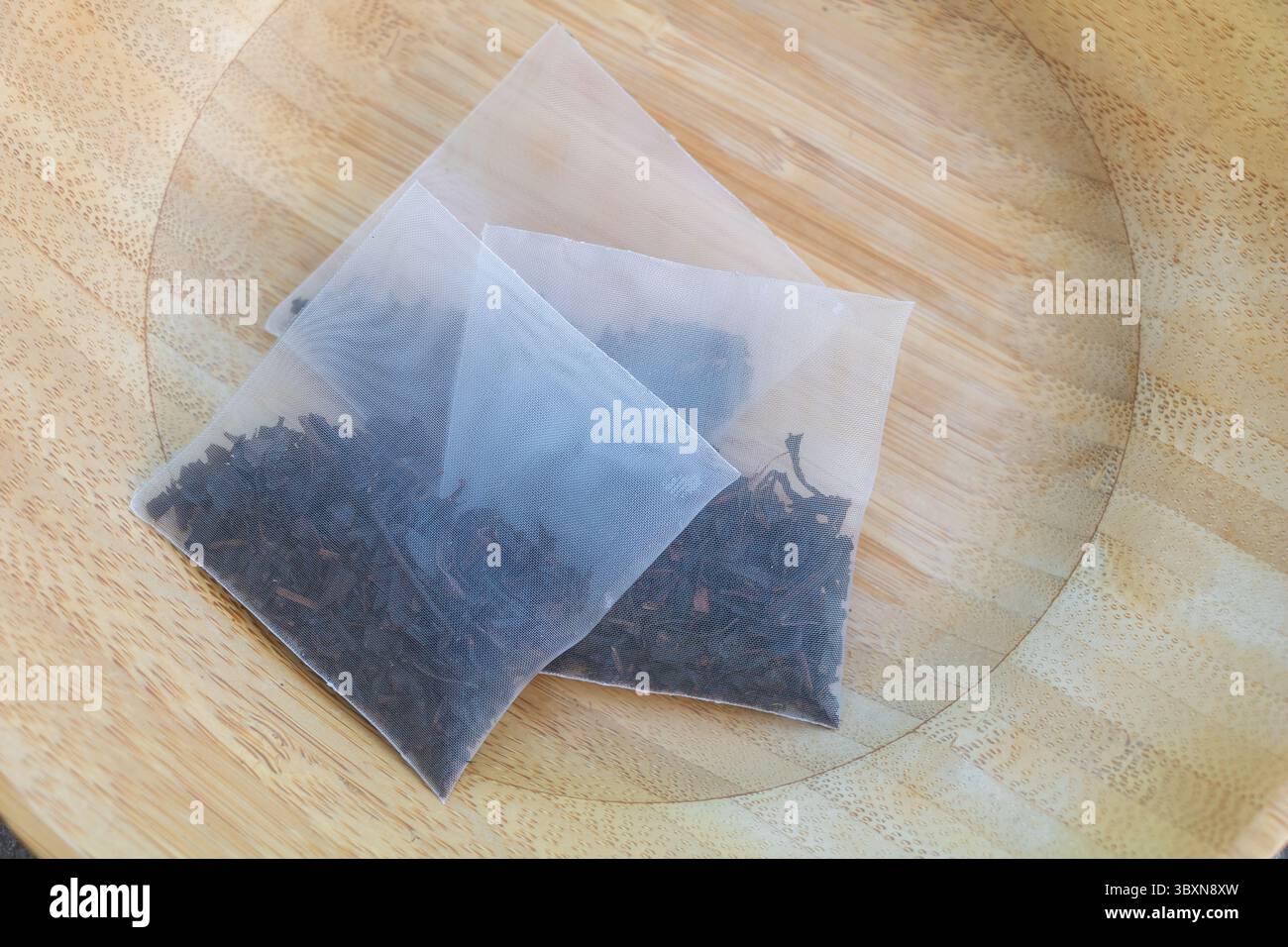 Primo piano delle sacche di tè nero a forma di piramide piene di tè sciolto con foglie su piatto di legno. Foto Stock